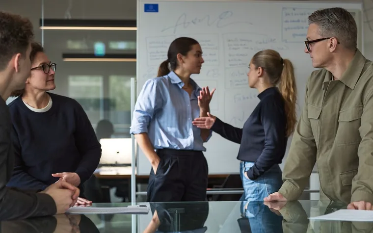 Four colleagues around a meeting table, working through a plan on a whiteboard behind them.